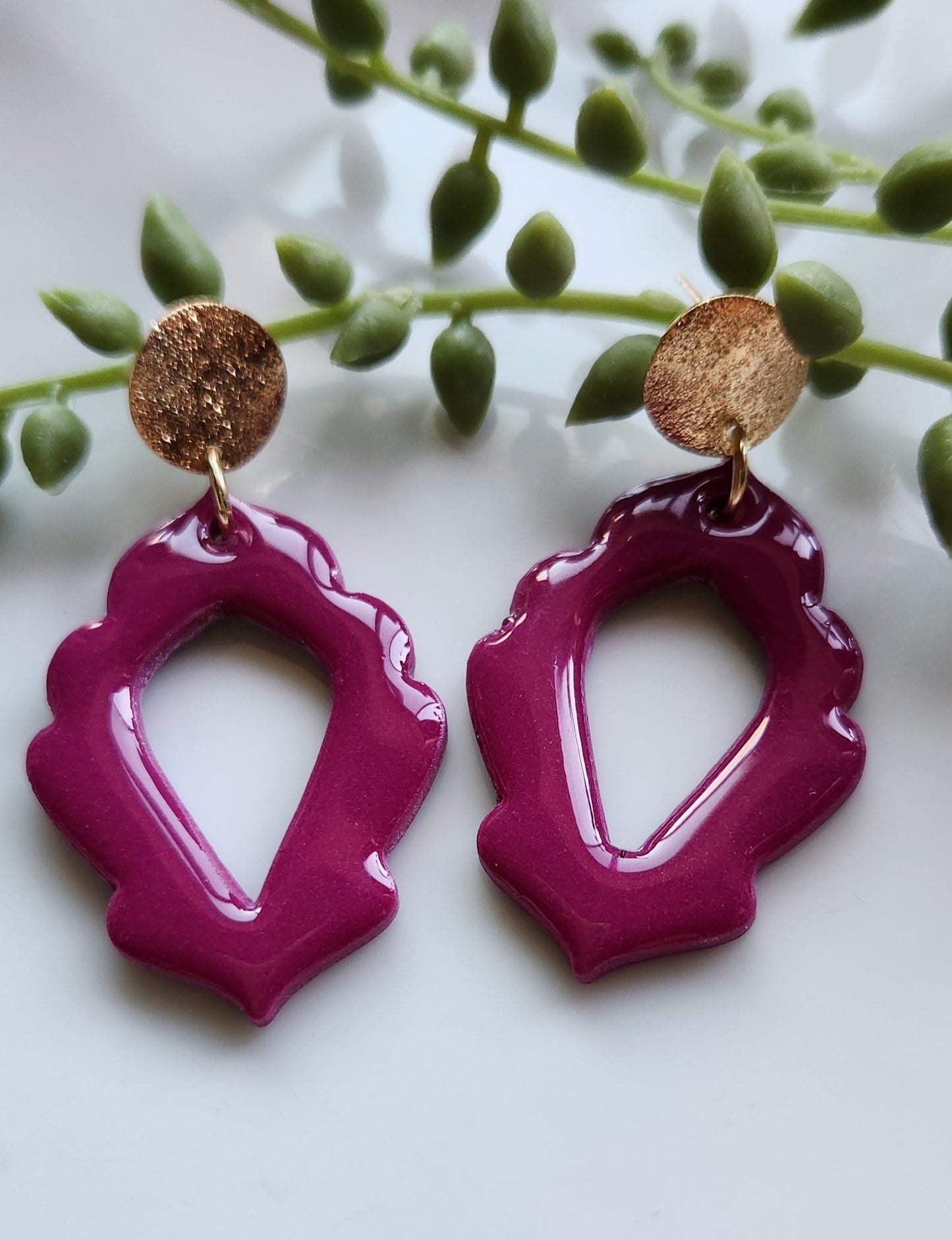 Handmade polymer clay earrings! Stunning fuchsia color clay mix creates this dangle. Design is an open oval shape with a floral border cutout and a shimmery gold plated circle stud completes this look. Lightweight and with resin for glossy finish. Approximately 2" long.