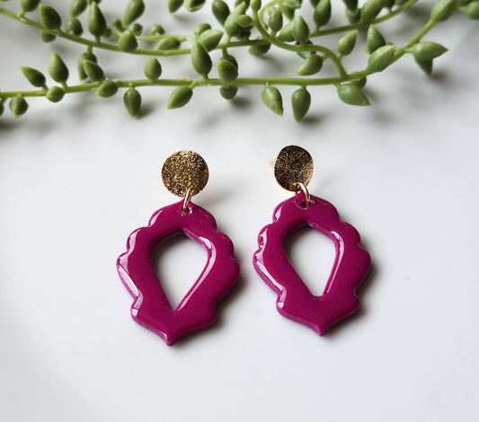 Handmade polymer clay earrings! Stunning fuchsia color clay mix creates this dangle. Design is an open oval shape with a floral border cutout and a shimmery gold plated circle stud completes this look. Lightweight and with resin for glossy finish. Approximately 2" long.