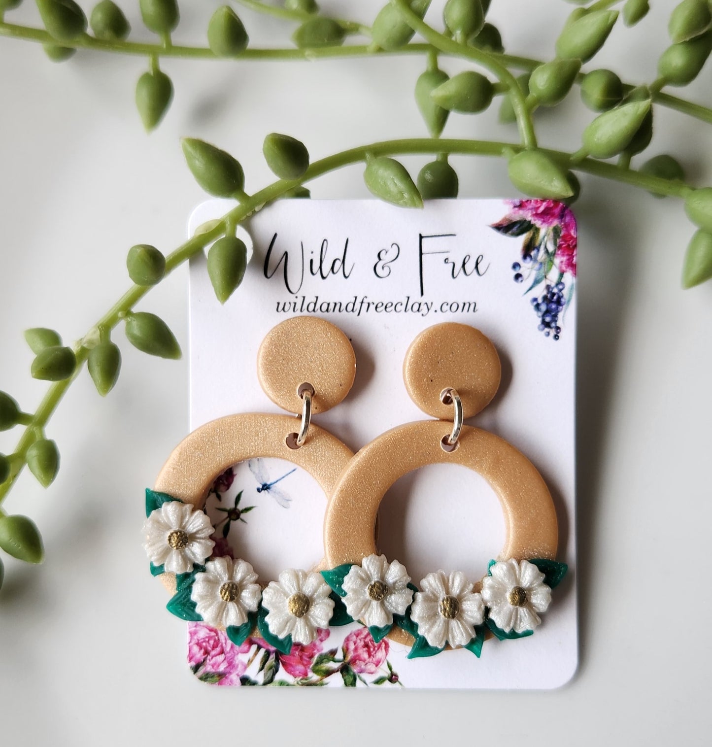 Handmade polymer clay earrings! Beautiful gold clay color with a small circle stud holding an open large circle. Large circle has three white flowers with green leaves in the background. Perfect jewelry piece with neutral colors styling any type of outfit! Lightweight and pproximately 1.5" long.