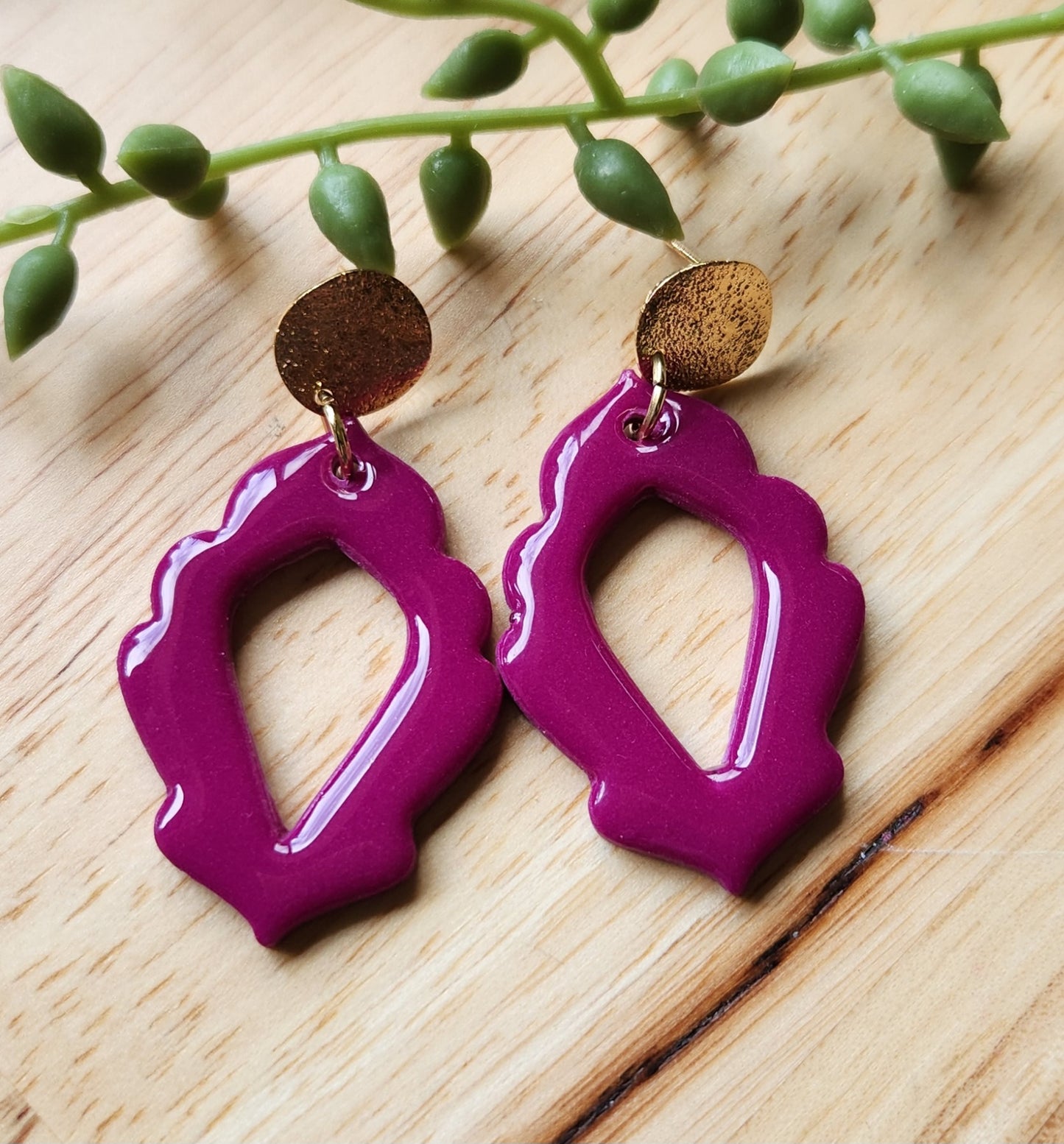 Handmade polymer clay earrings! Stunning fuchsia color clay mix creates this dangle. Design is an open oval shape with a floral border cutout and a shimmery gold plated circle stud completes this look. Lightweight and with resin for glossy finish. Approximately 2" long.