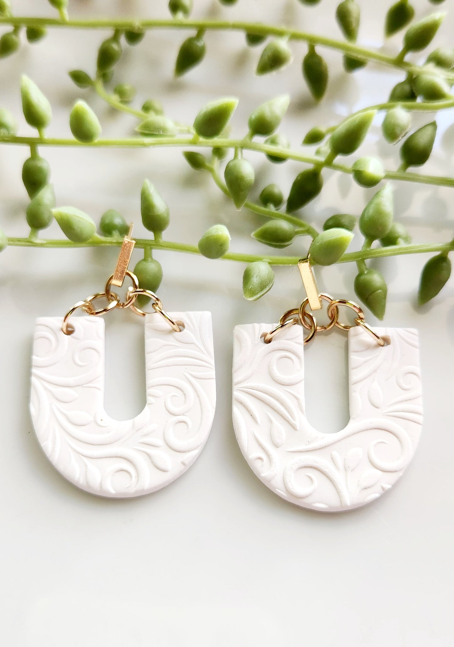 Handmade polymer clay earrings! Beautiful, bold, lightweight clay earrings! These earrings are designed in a u shape with white clay as a base and textured as vines throughout. A gold plated skinny rectangle is used as a stud to complete this beautiful piece. Matte look and approximately 2" long.