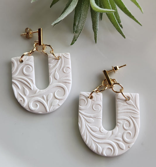 Handmade polymer clay earrings! Beautiful, bold, lightweight clay earrings! These earrings are designed in a u shape with white clay as a base and textured as vines throughout. A gold plated skinny rectangle is used as a stud to complete this beautiful piece. Matte look and approximately 2" long.