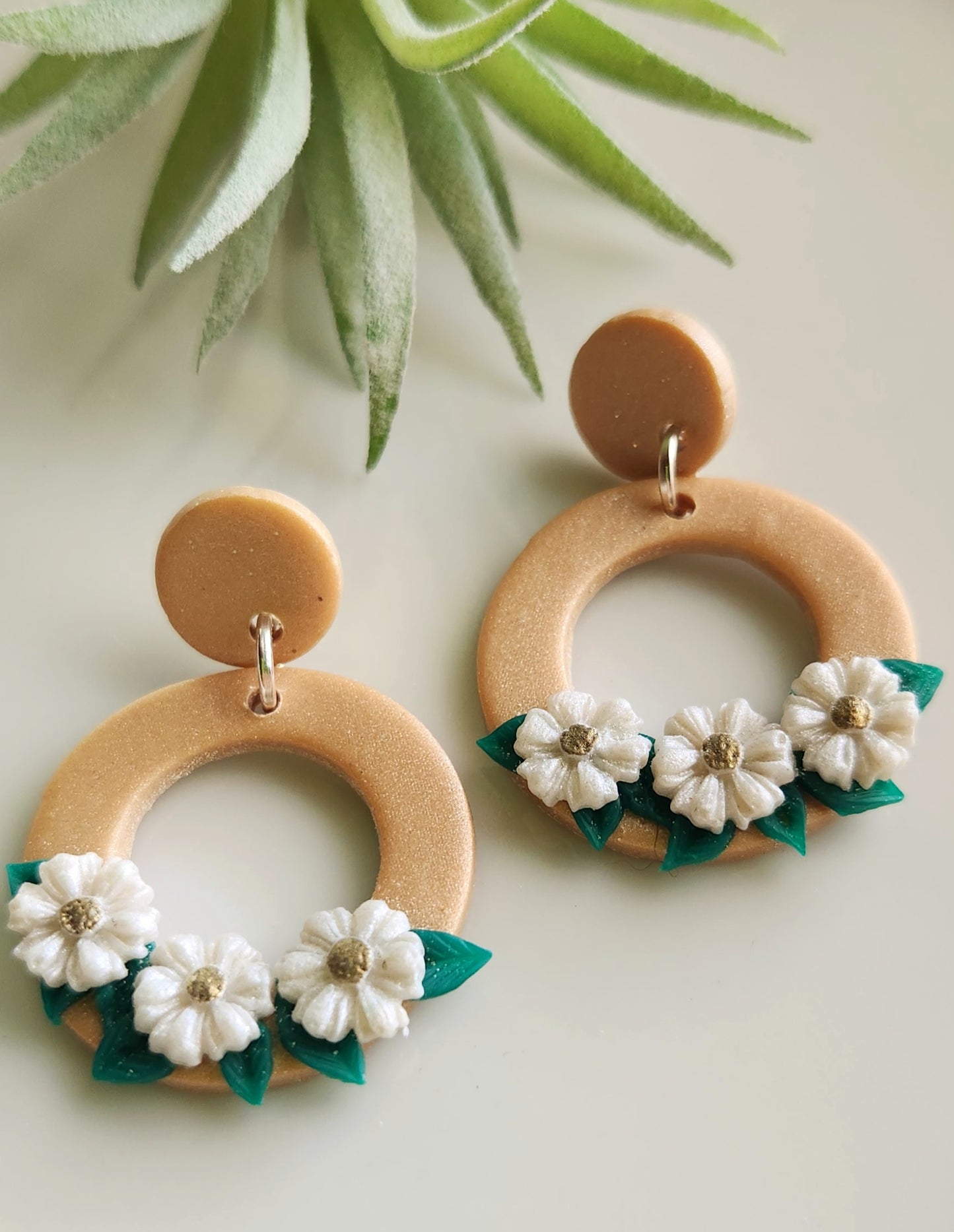 Handmade polymer clay earrings! Beautiful gold clay color with a small circle stud holding an open large circle. Large circle has three white flowers with green leaves in the background. Perfect jewelry piece with neutral colors styling any type of outfit! Lightweight and pproximately 1.5" long.