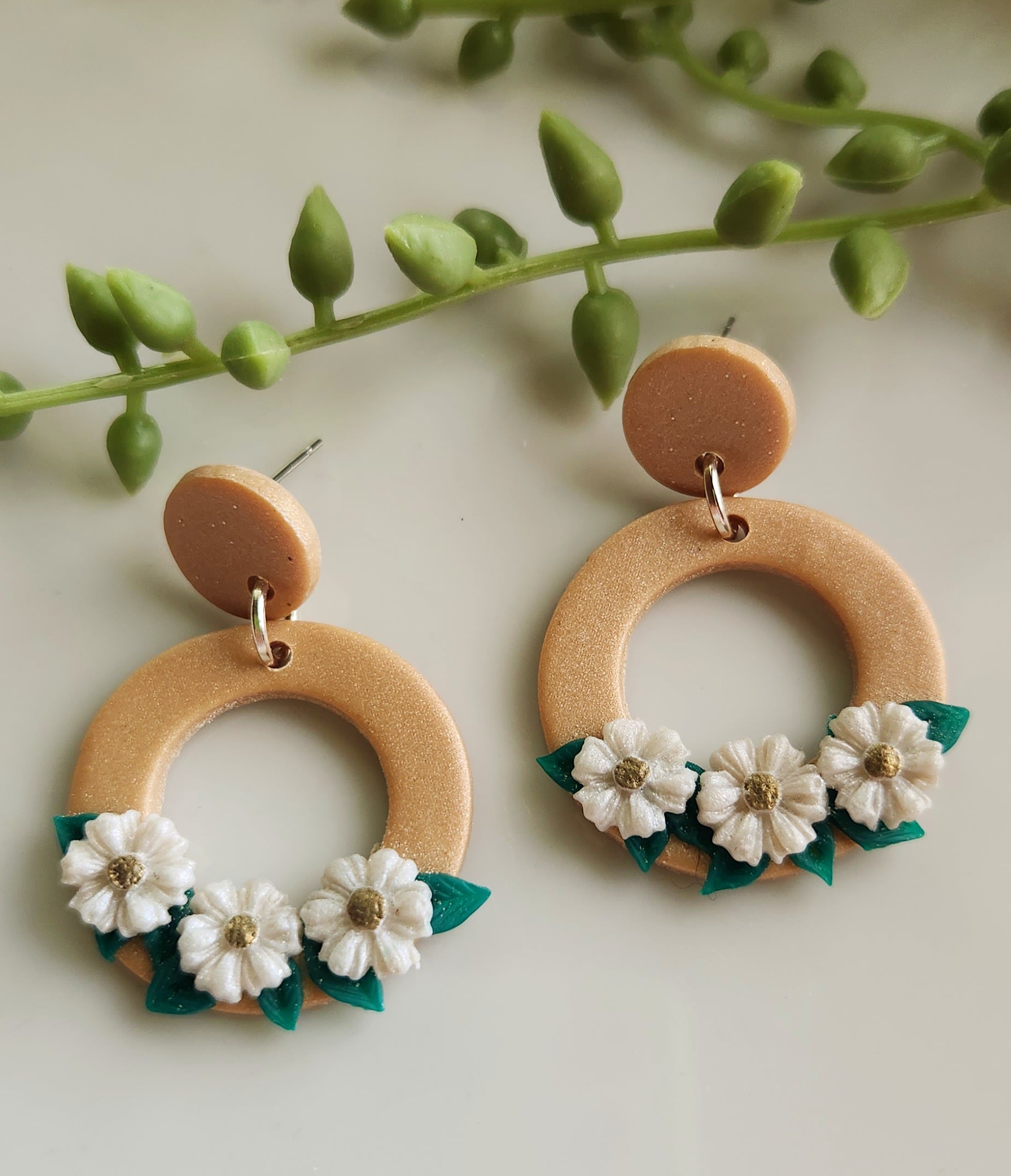 Handmade polymer clay earrings! Beautiful gold clay color with a small circle stud holding an open large circle. Large circle has three white flowers with green leaves in the background. Perfect jewelry piece with neutral colors styling any type of outfit! Lightweight and pproximately 1.5" long.