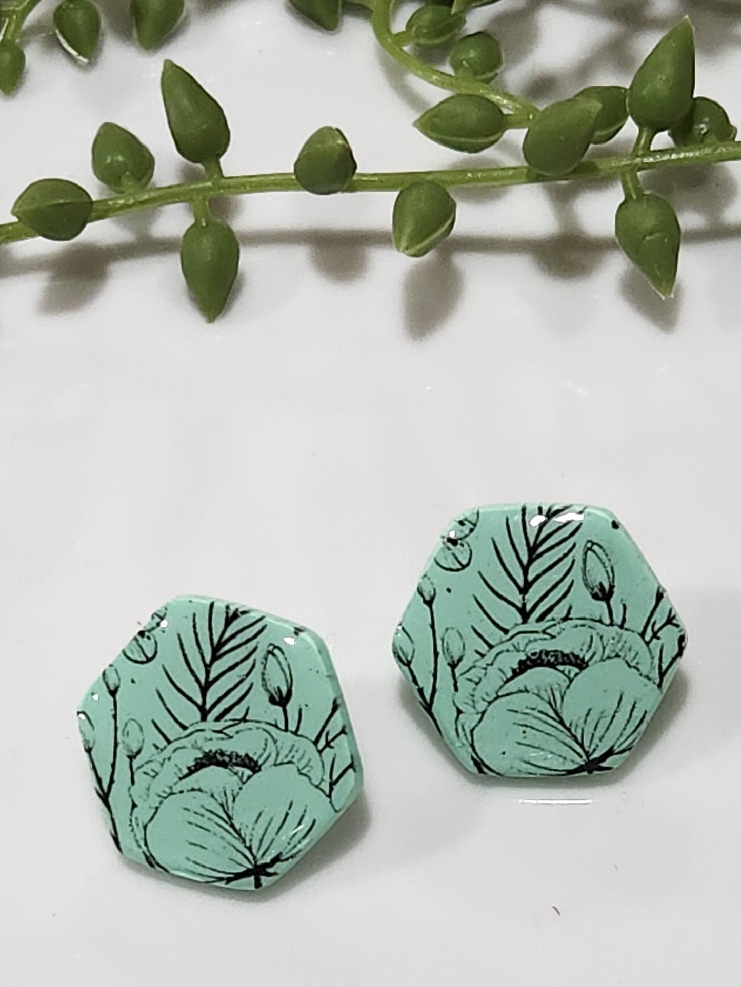 Handmade polymer clay earrings! Hexagon shape stud with mint background clay and black floral design paint. These stud earrings are perfect for any outfit and a staple accessory item for all. Studs are approximately 1" long and with resin for a glossy look.