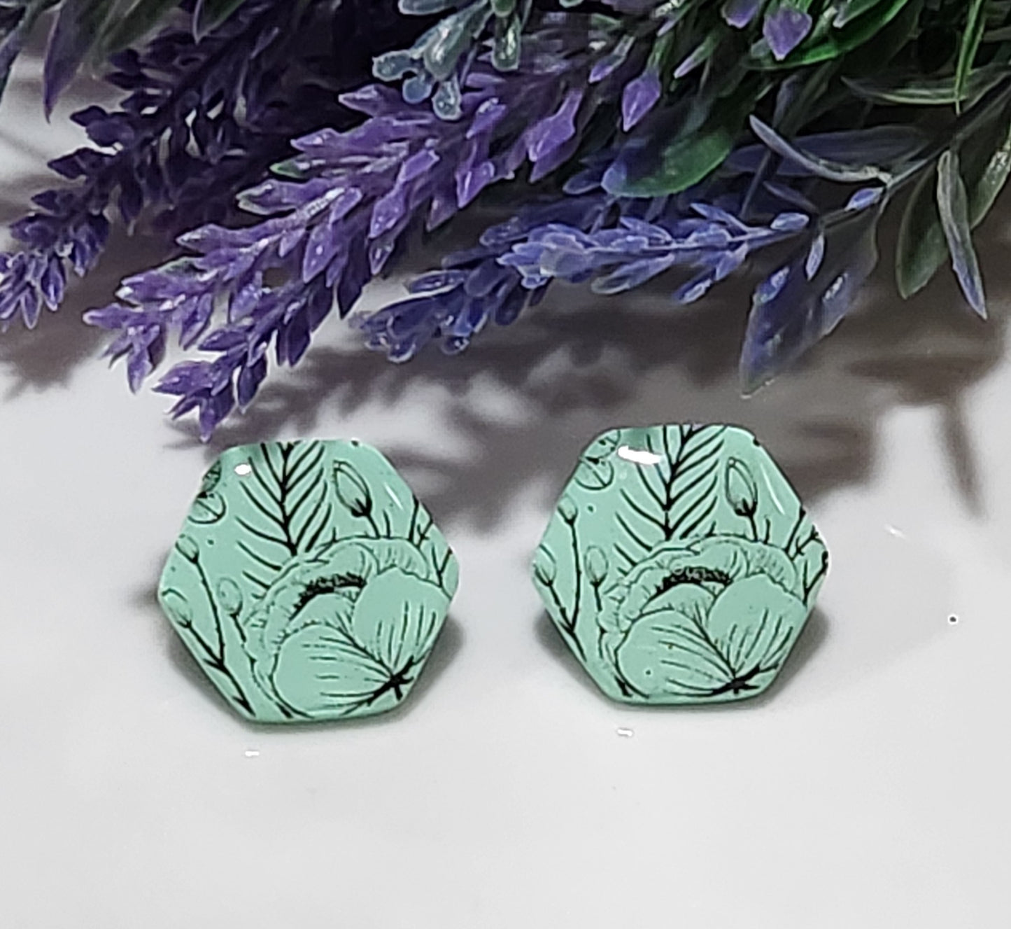 Handmade polymer clay earrings! Hexagon shape stud with mint background clay and black floral design paint. These stud earrings are perfect for any outfit and a staple accessory item for all. Studs are approximately 1" long and with resin for a glossy look.