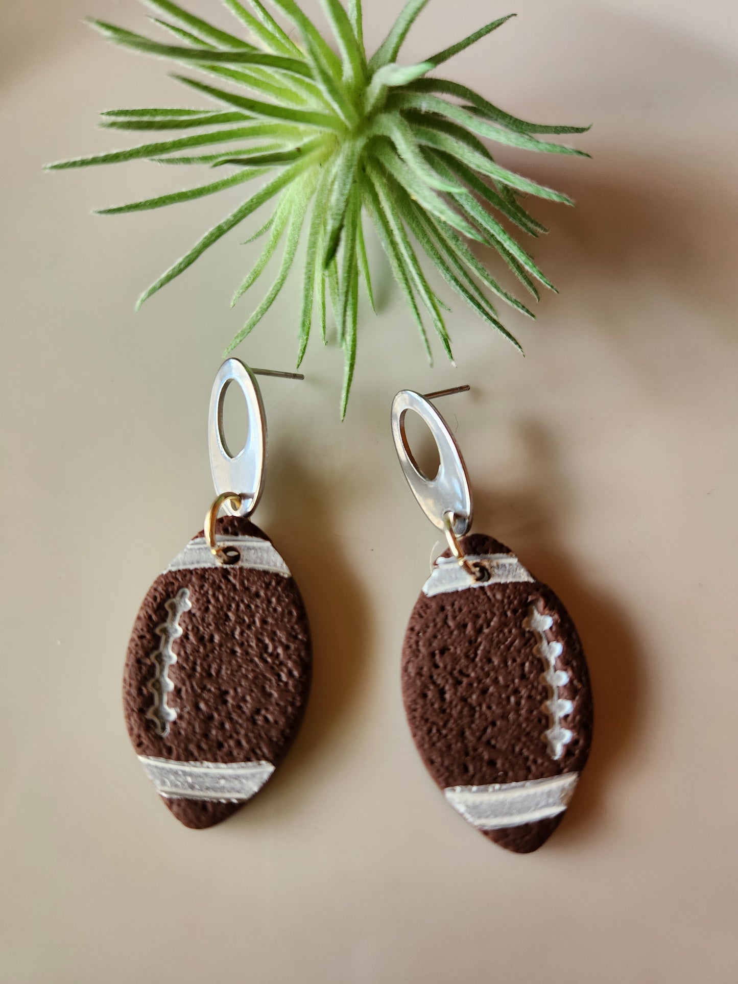 Handmade polymer clay football earrings! Be gameday-ready with these beautiful football earrings! No matter what your team is you are sure to stand out with these lightweight football dangles. These earrings are cut like a football shape with brown color clay. White paint highlights the ball design. They are textured matte with silver-plated open oval studs. Approximately 2" long.