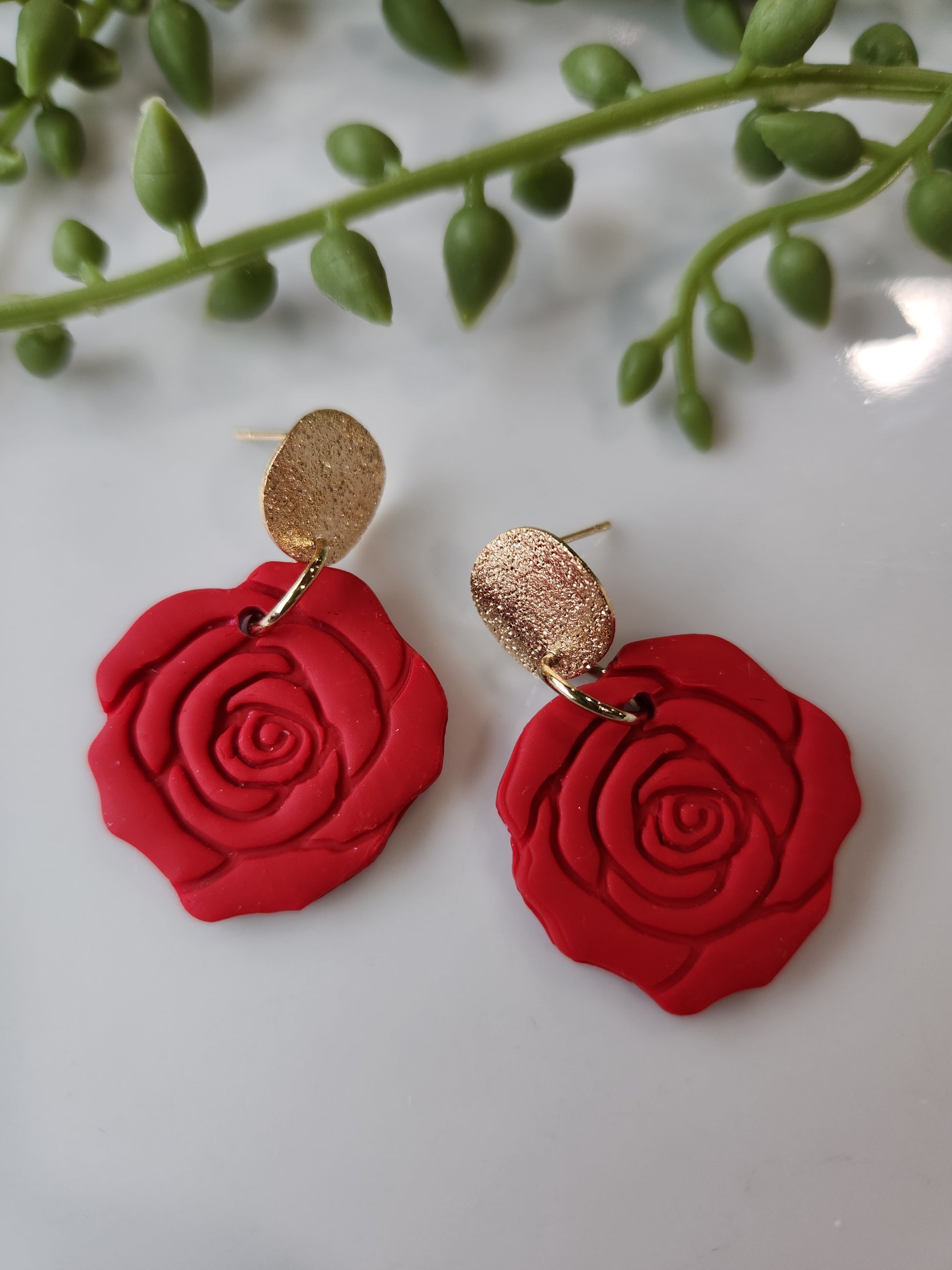 Handmade polymer clay earrings! These beautiful clay dangles are of a rose design with two different colors, red and red wine. They are matte with a shimmery gold-plated circle stud. Lightweight and approximately 1.5" long.