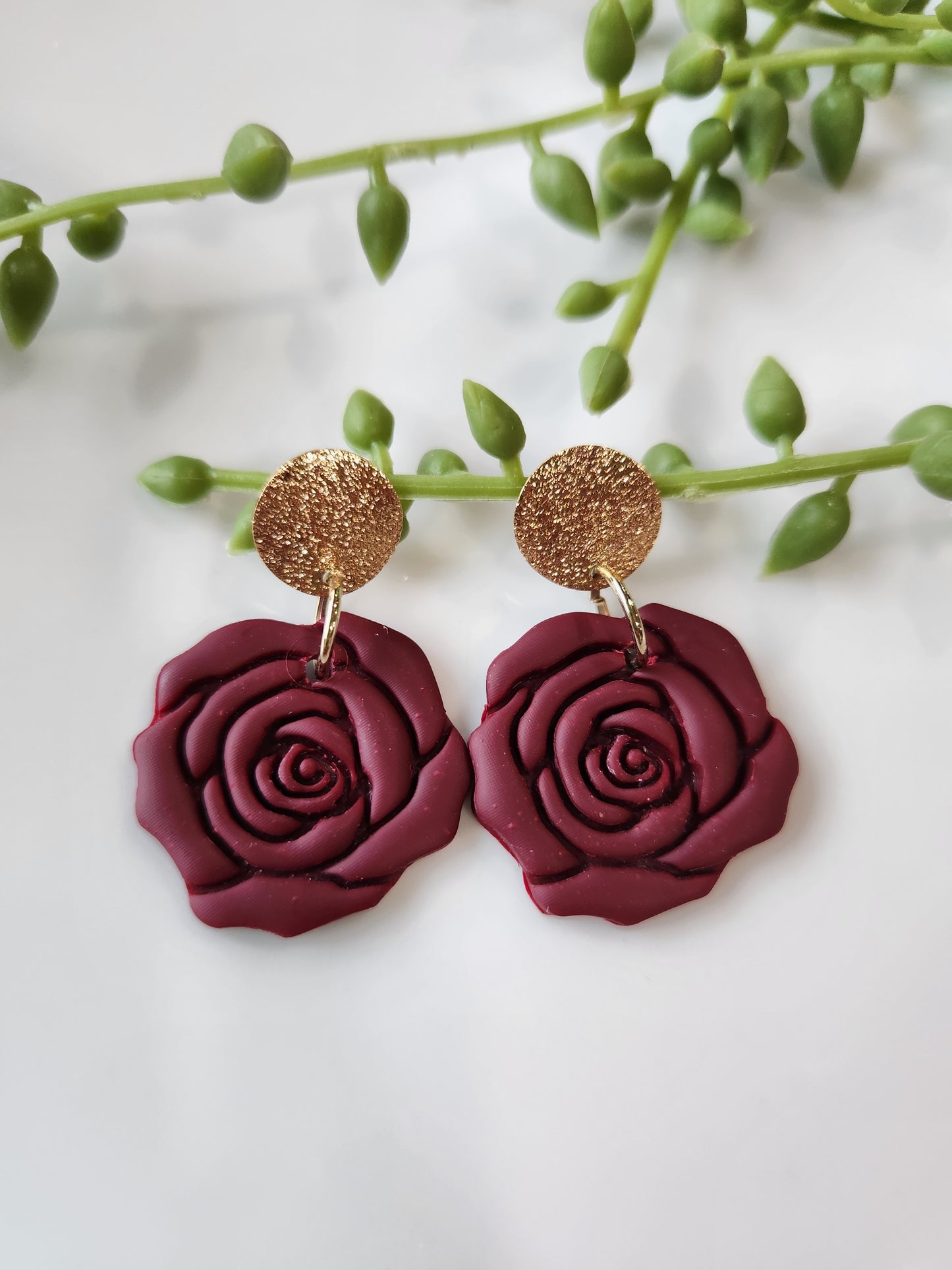 Handmade polymer clay earrings! These beautiful clay dangles are of a rose design with two different colors, red and red wine. They are matte with a shimmery gold-plated circle stud. Lightweight and approximately 1.5" long.