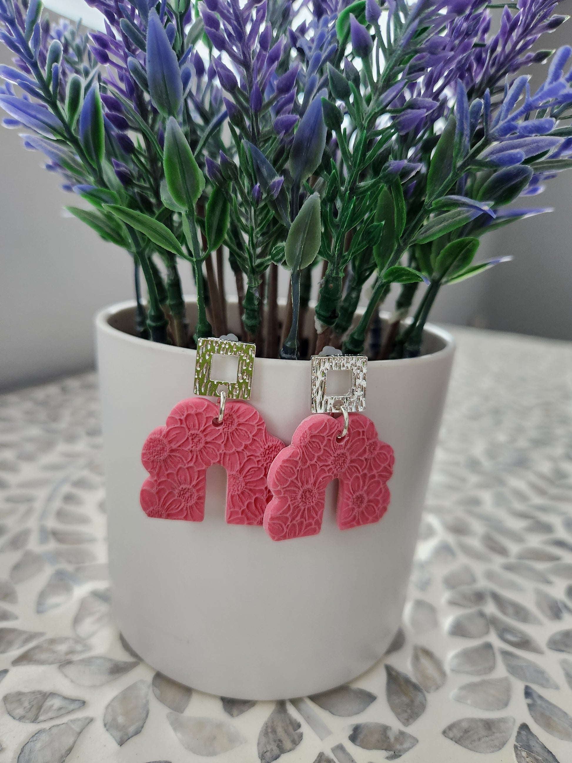 Handmade polymer clay earrings! These beautiful earrings are made of pink clay and with a scalloped-shaped design. They are textured with floral print throughout and with an open square silver plated stud. They are matte, lightweight, and approximately 2" long.