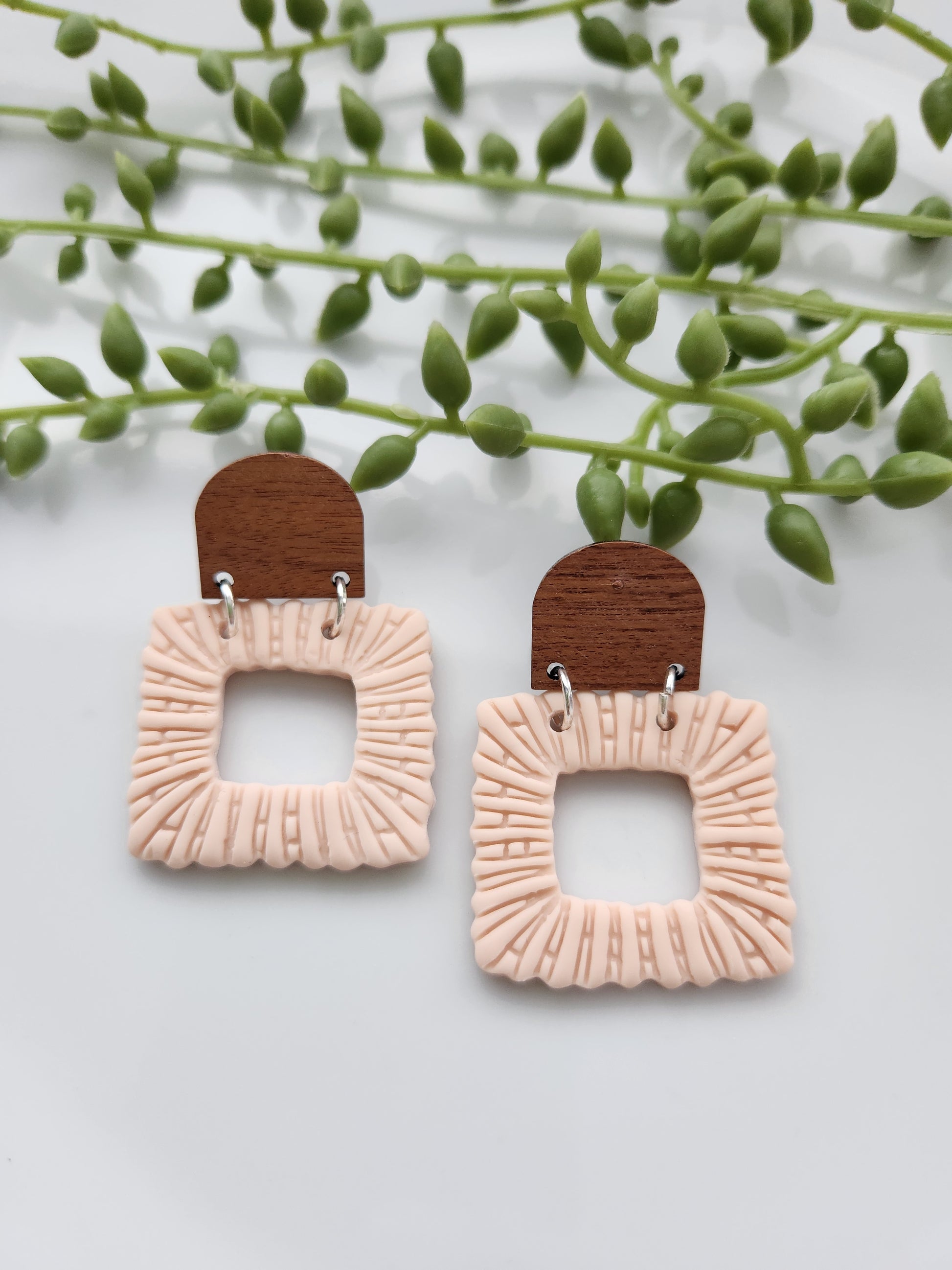 Handmade polymer clay blush earrings! These beautiful earrings are made out of polymer clay in a light blush color. They are square-shaped with an open square in the middle. The dome-shaped wood stud completes this dangle earring. These earrings are textured, lightweight, and approximately 2" long.