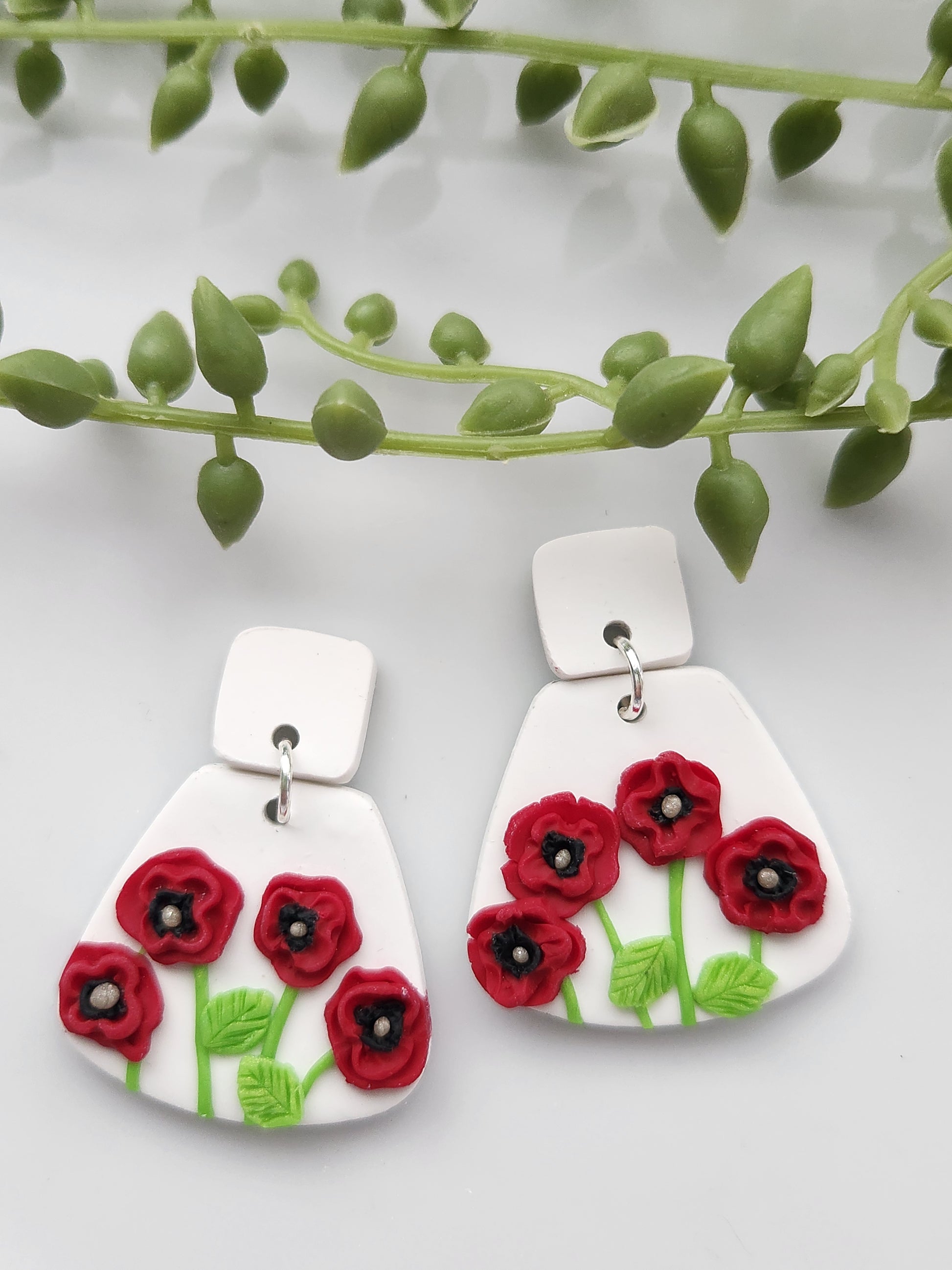 Handmade polymer clay earrings! These unique red poppy flower earrings are sure to stand out! White clay is the base of these earrings with four red poppy flowers. A white clay small square is used as a stud. Lightweight and approximately 1.5" long.