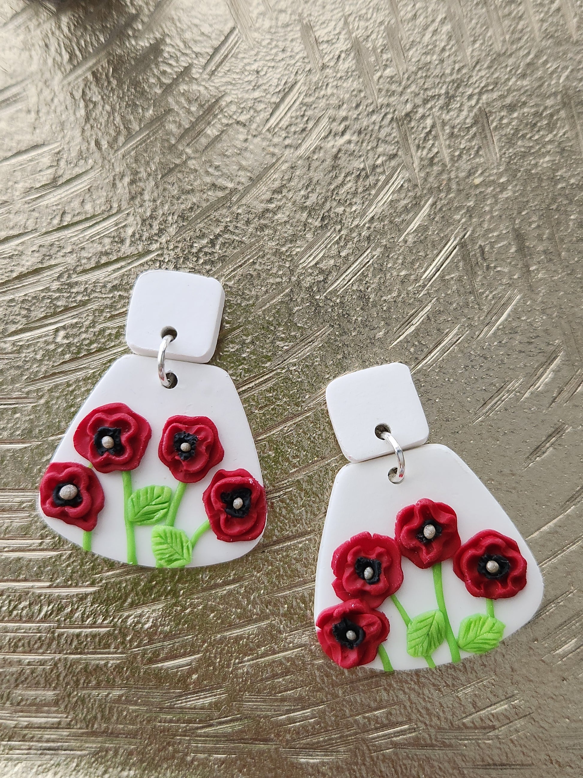 Handmade polymer clay earrings! These unique red poppy flower earrings are sure to stand out! White clay is the base of these earrings with four red poppy flowers. A white clay small square is used as a stud. Lightweight and approximately 1.5" long.