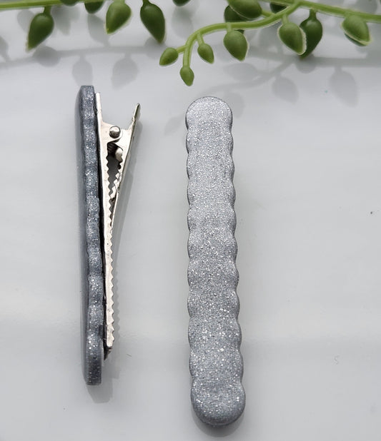 Handmade polymer clay hair clips! Super lightweight clips that bring a pop to any outfit! This beautiful clip is handmade with polymer clay in a shimmery silver color. The hair clip has a scalloped cutout and is layered with a coat of resin for a shiny look. Approximately 2.5" long.