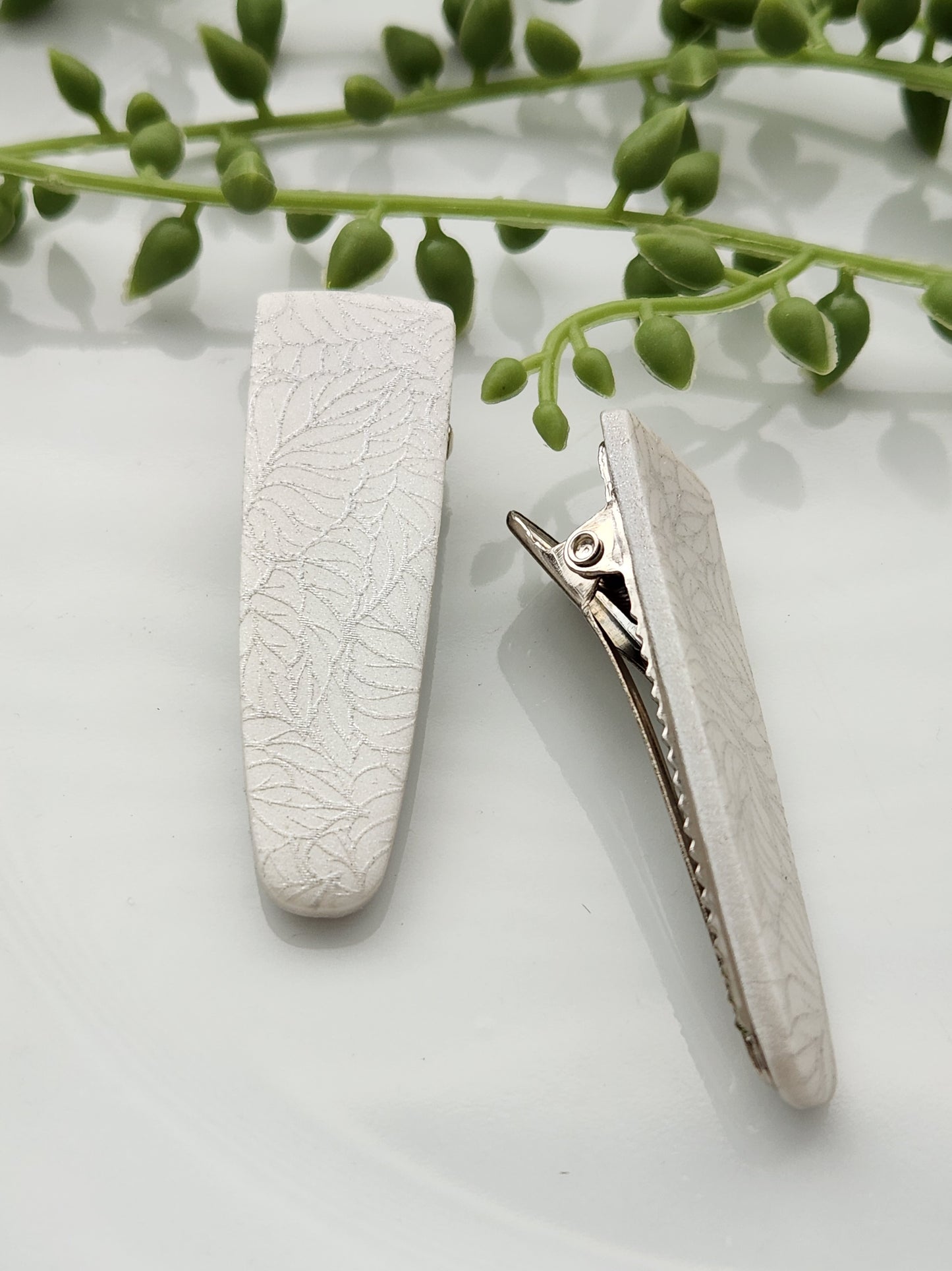 Handmade polymer clay hair clips! Super lightweight clips that bring a pop to any outfit! This beautiful clip is handmade with a polymer clay shimmery pearl color. The hair clip is a teardrop shape and with a silver leave print. It is matte and approximately 2.5" long.