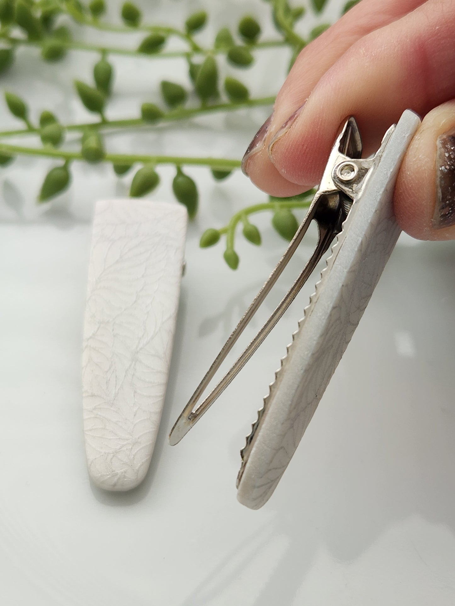 Handmade polymer clay hair clips! Super lightweight clips that bring a pop to any outfit! This beautiful clip is handmade with a polymer clay shimmery pearl color. The hair clip is a teardrop shape and with a silver leave print. It is matte and approximately 2.5" long.