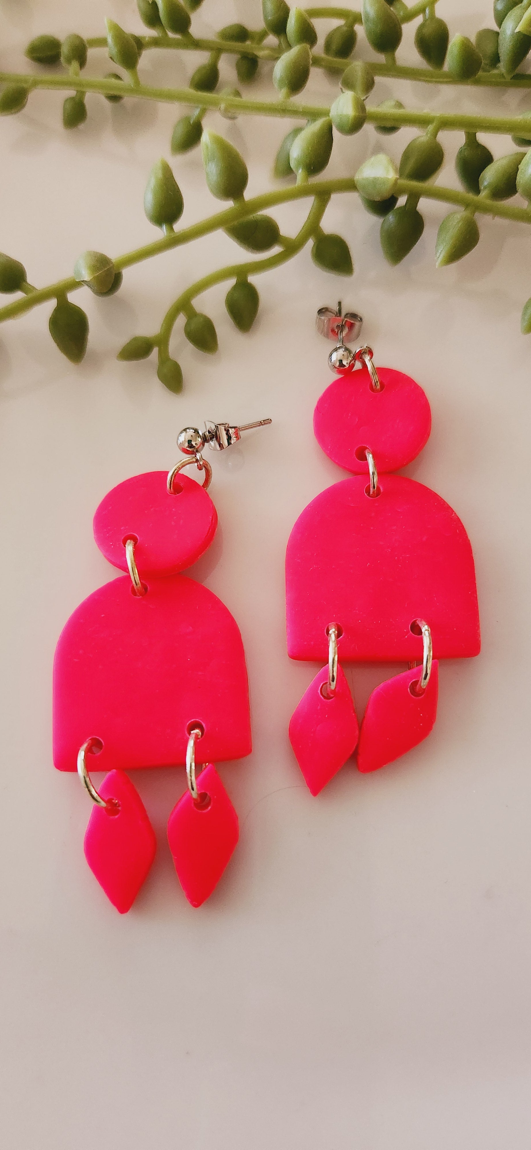 Handmade polymer clay earrings! These stunning hot pink clay earrings are sure to stand out. They consist of a clay circle with a half dome and two small diamond-shaped dangles. A circle ball stud completes this look. They are lightweight and approximately 2.5" long.