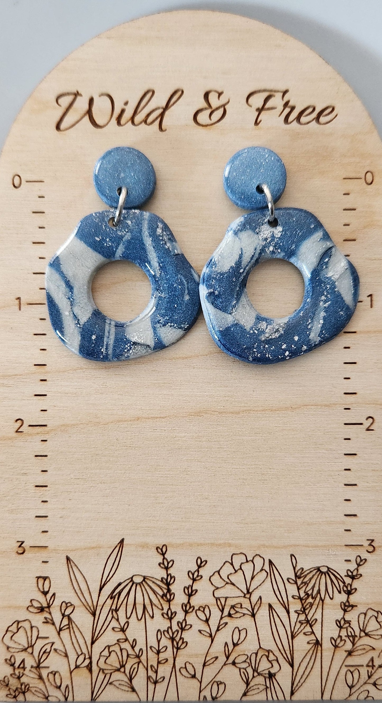 This handmade polymer clay earring is a blend of blue, white and silver colors, and its lightweight structure is coated with a glossy resin finish. Designed with an abstract open circle shaped dangle and a solid circle stud.  Approximately 1.5" long.