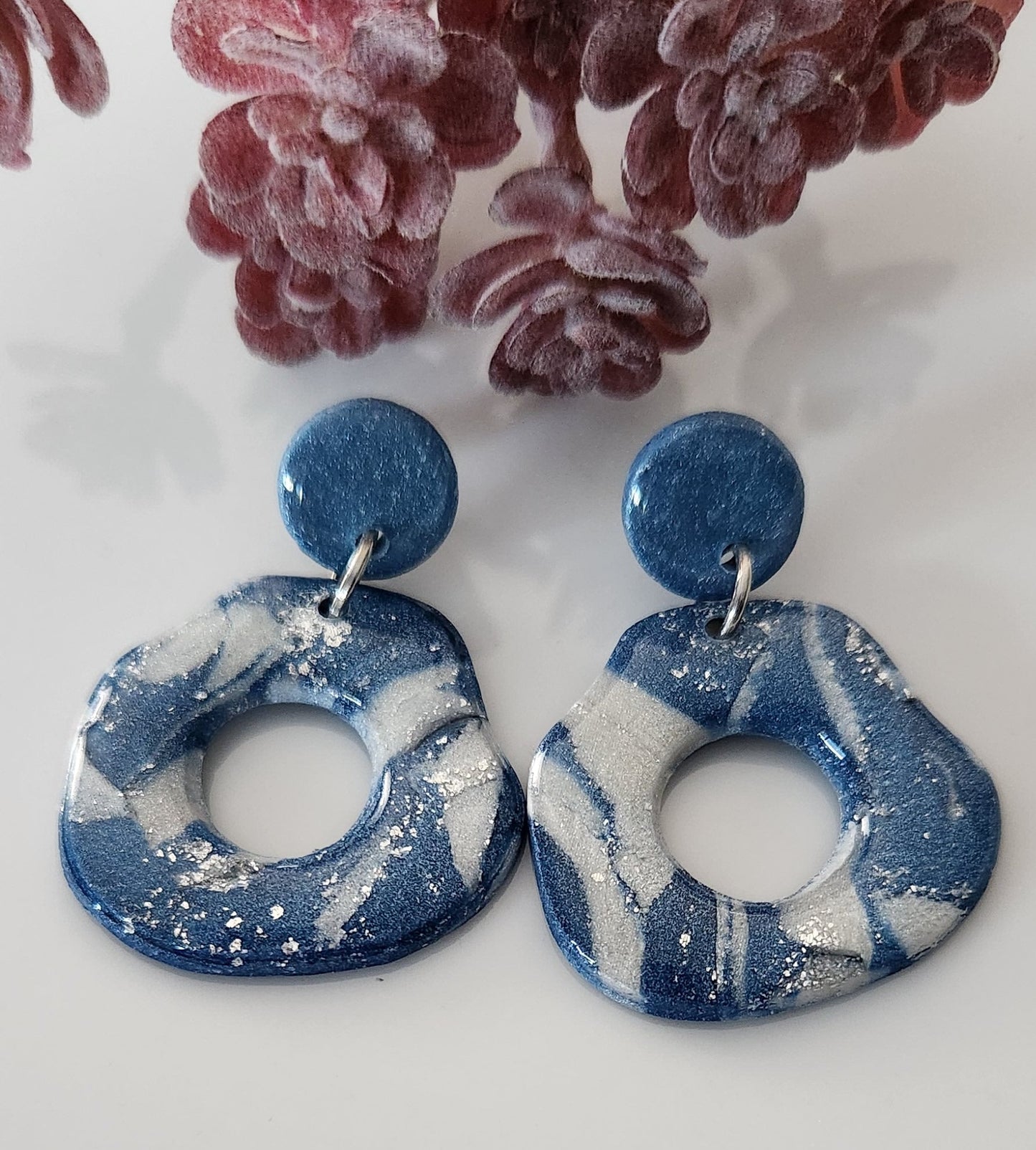 This handmade polymer clay earring is a blend of blue, white and silver colors, and its lightweight structure is coated with a glossy resin finish. Designed with an abstract open circle shaped dangle and a solid circle stud.  Approximately 1.5" long.